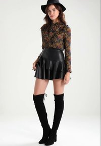 Saia mini em couro preto, com corte evasê e bainha franzida, combinada com uma blusa de manga longa estampada. O modelo usa botas de camurça pretas até o joelho e um chapéu.