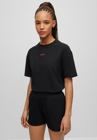 Black cotton t-shirt and shorts set. T-shirt has short sleeves and red "HUGO" logo. Shorts feature an elastic waistband and slight sheen.