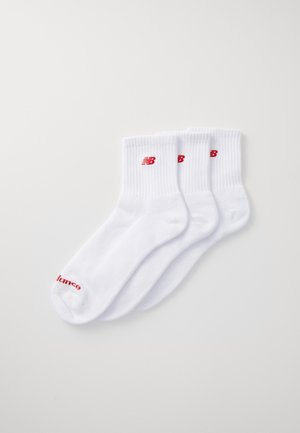 Calcetines de algodón blancos de corte crew con puños acanalados. El logo de New Balance está impreso en rojo en el tobillo, con la palabra "balance" también en rojo cerca de los dedos.