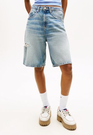 Inimene, kes kannab helerohelisi põlvikuni ulatuvaid teksapükse, millel on vasakul reiel väike rebend, valgeid sokke ja valgete paksu tallaga jalanõusid.