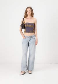 Top corto gris con estampado gráfico, combinado con jeans de pierna ancha azul claro y zapatos tipo slip-on beige. Un pequeño bolso negro acentúa el atuendo.