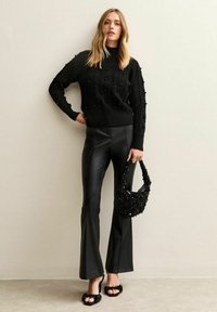 Maglione nero lavorato a maglia con pois in rilievo, abbinato a pantaloni neri lucidi a zampa d'elefante. Accessoriato con una borsa nera di perline e sandali pelosi.