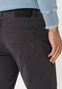Grijze katoenen broek met een achterzak, voorzien van een subtiel stikselontwerp. Een zwart merketiket is zichtbaar bij de tailleband.