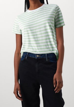 Maglietta a righe verde chiaro e bianco, realizzata in materiale morbido. Maniche corte, colletto girocollo. Abbinata a jeans neri a vita alta.