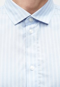 Jasnoniebieska koszula w białe pionowe paski, z kołnierzykiem na guziki i białymi guzikami. Gładka tkanina o delikatnym połysku.
