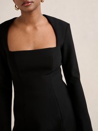 Schwarzes Kleid mit langen Ärmeln, quadratischem Ausschnitt, figurbetontem Oberteil und glatter Textur. Verfügt über klare Linien und ein minimalistisches Design.