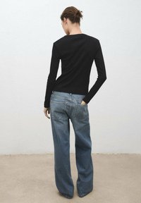 Zwarte lange mouwen top en lichtblauwe wijde jeans. Top met een ronde hals; jeans hebben een klassiek vijf-pocket ontwerp.