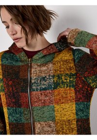 Kardigan z kapturem z wielokolorowym wzorem w stylu patchworku w ziemistych odcieniach, wykonany z teksturowanej dzianiny, z zamkiem błyskawicznym z przodu.