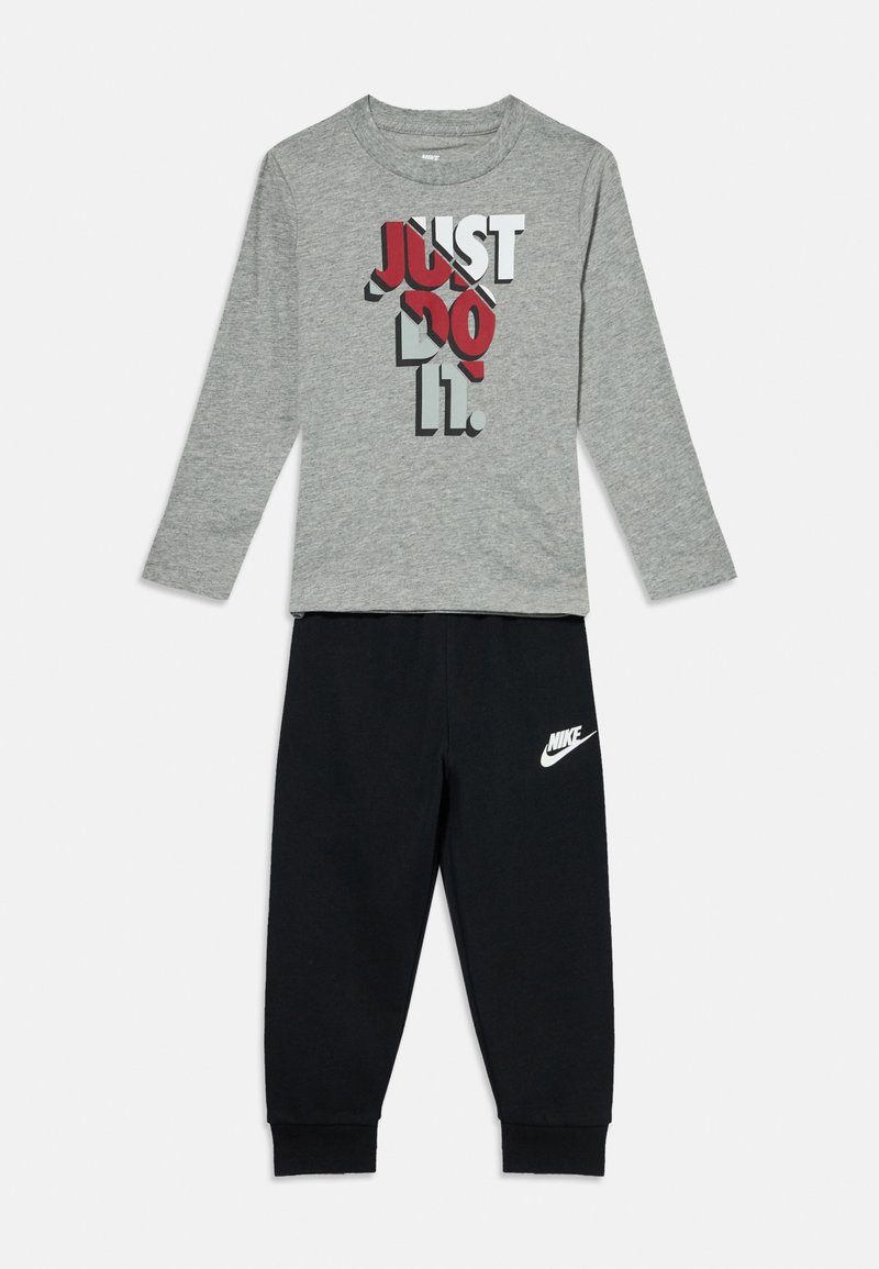 Szara koszula z długim rękawem z grafiką "JUST DO IT" w kolorze czerwonym i czarnym, zestawiona z czarnymi dresami z białym logo Nike.