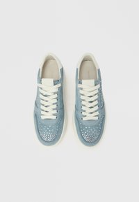 Svetlo modri semišasti supergi z belimi vezalkami in teksturirano gumijasto podplatom. Okrašeni so z dekorativnimi kristalčki na prednjem delu in ob straneh.