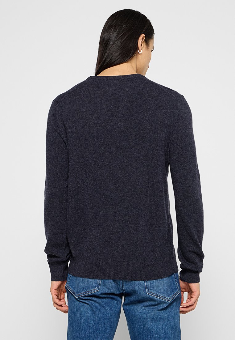 Marineblauer Rundhalsausschnitt-Pullover mit langen Ärmeln, weichem Material und gerippten Bündchen und Saum, kombiniert mit Jeans.