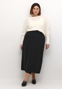 Ivory sweater met gestructureerde mouwen, gecombineerd met een zwarte wikkelrok tot de enkel. Zwarte flats maken de outfit compleet. Eenvoudig, elegant ontwerp.