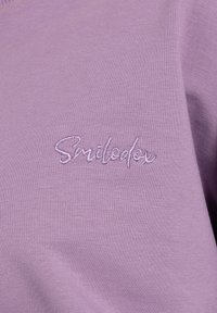 Maglione viola chiaro con una texture morbida e logo ricamato "Smilodex" in una tonalità contrastante. Design semplice e casual.