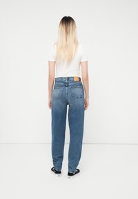 Μπλε τζιν παντελόνι με χαλαρή εφαρμογή, διαθέτοντας μια καφέ δερμάτινη επιφάνεια στη πίσω μέση και δύο πίσω τσέπες. Ίσιο, απλό μπροστινό μέρος.