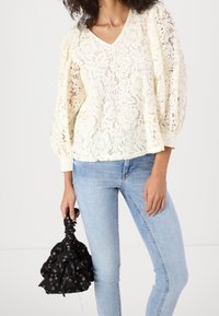 Spetsblus i off-white med V-ringning och puffärmar. Matchad med ljusblå jeans och en svart blommig dragsko-väska.