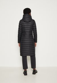 Černý vycpaný dlouhý kabát s kapucí, se švy uspořádanými horizontálně a přiléhavým střihem. Nosit s černými kalhotami a botami.