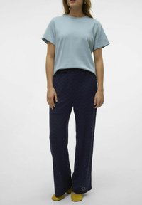 Vaaleansininen lyhythihainen t-paita, tummansinisiä chevron-kuosisia housuja ja keltaisia ballerinoja. Housuissa on karkea, rei'itetty kuosi.