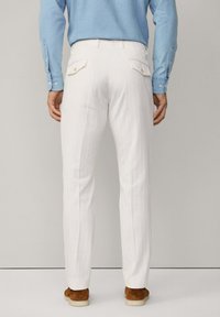 Pantalons blancs avec une coupe droite, dotés de deux poches arrière et de rayures discrètes. Associés à une chemise bleu clair et des chaussures marron.