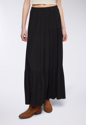 Gonna maxi nera con design a strati, vita elastica e tessuto morbido, abbinata a stivali alla caviglia marroni con tacco basso.