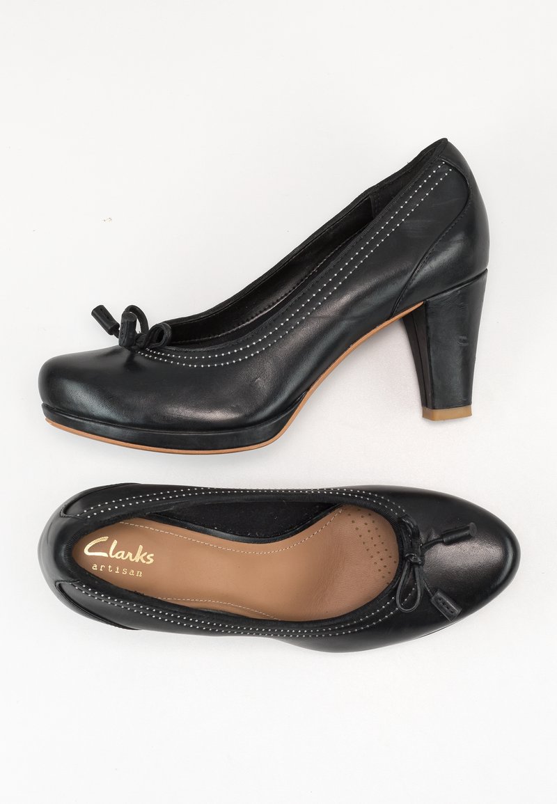 Chaussures à talons en cuir noir avec un bout arrondi et des coutures décoratives. Elles présentent un nœud sur le devant et une semelle intérieure texturée.