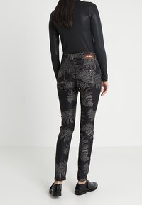 Černé džíny s komplikovanými stříbrnými vzory kapradin, slim-fit design a hnědou koženou nášivkou na zadní straně. Hladká textura s těsným tkaním.