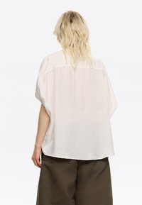 Leichte, locker sitzende Bluse aus einem weichen, cremigen Stoff. Kurze Ärmel, ein abgerundeter Saum und eine entspannte Silhouette sorgen für lässigen Komfort.
