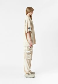 Camiseta de corduroy beige de corte oversize y pantalones cargo a juego con múltiples bolsillos, combinados con zapatos de slip-on de textura gris.