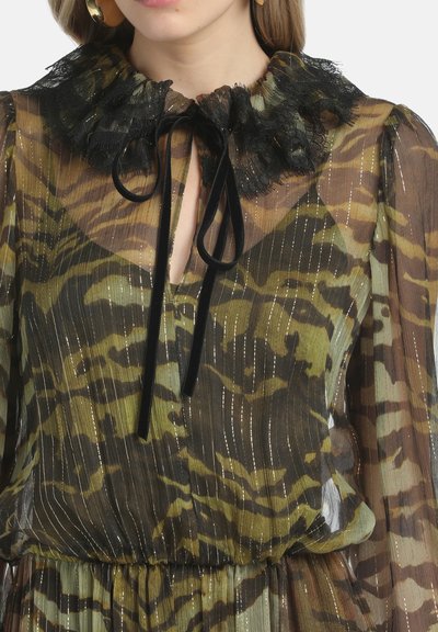 Durchsichtige Bluse mit langen Ärmeln, die grüne und braune Tigerstreifen, metallische vertikale Streifen, einen Kragen aus schwarzer Spitze und schwarze Samt-Bänder hat.