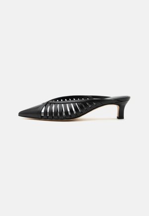 Mule en cuir noir avec bout pointu, design découpé à brides et petit talon kitten sur fond blanc.