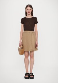 Brown knitted top, beige linen wrap skirt, black platform sandals, and a woven wooden handbag. Simplistic, contemporary design with clean lines.