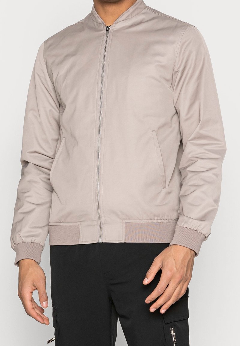 Lichtgrijze bomberjack van soepel materiaal, met een frontzipper, zijzakken en ribgebreide cuffs en zoom. Minimalistisch ontwerp.
