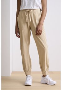 Helle beige, konisch zulaufende Hosen aus einem strukturierten Stoff, mit einem elastischen Bund und Kordelzug, seitlichen Taschen und gerafften Bündchen.