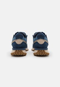 Navy blue suede sneakers with beige accents, featuring a rubber outsole and pull tabs. Closed design with a reinforced heel.