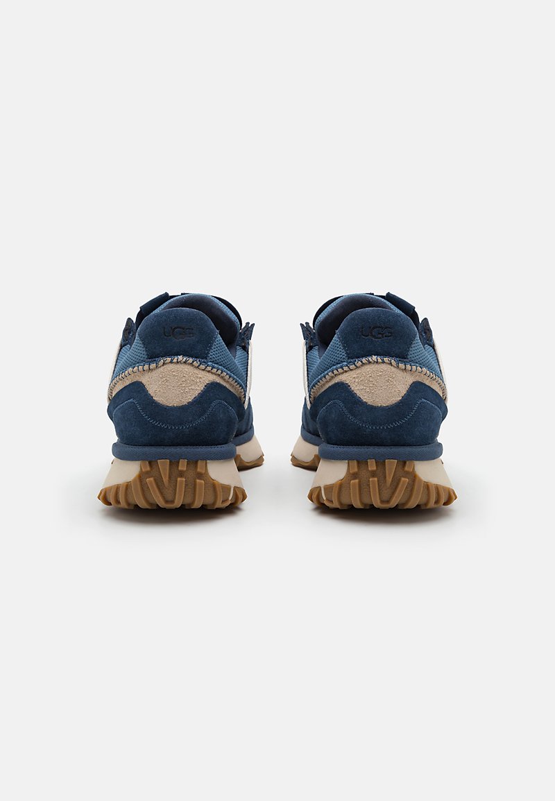 Marineblauwe suède sneakers met beige accenten, voorzien van een rubberen zool en treklussen. Gesloten ontwerp met een versterkte hiel.