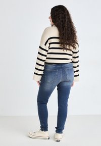 Beige and black striped sweater, relaxed fit, worn with blue skinny jeans. Jeans feature a faded wash and subtle back pockets, paired with sneakers.