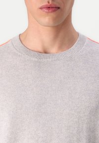 Pull en maille gris avec un col ras du cou, doté d'accents orange sur les épaules, fabriqué avec un matériau doux et d'une texture lisse.