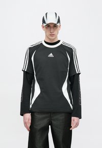 Fekete-fehér Adidas sportöltözet, rövid ujjú felsővel, alatta hosszú ujjúval, valamint egy hozzáillő sapkával és sötét nadrággal.