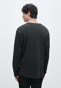 Langärmeliges, dunkelgraues Hemd aus weichem Stoff mit lockerem Schnitt, weitem Ausschnitt und seitlichen Schlitzen am Saum für zusätzlichen Komfort.