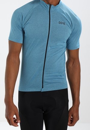 Uomo che indossa una maglia da ciclismo a maniche corte azzurro chiaro con una cerniera frontale nera e pantaloncini da ciclismo neri.