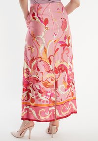 Lange roze rok van zijden stof met kleurrijke bloemmotieven in oranje, rood en crème, met een zijsplit en zakken.