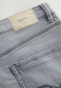 Jeans din denim cu o spălare gri deschis, având un patch din piele cu eticheta "DENIM SUPPLY", cusături vizibile și buzunare standard.