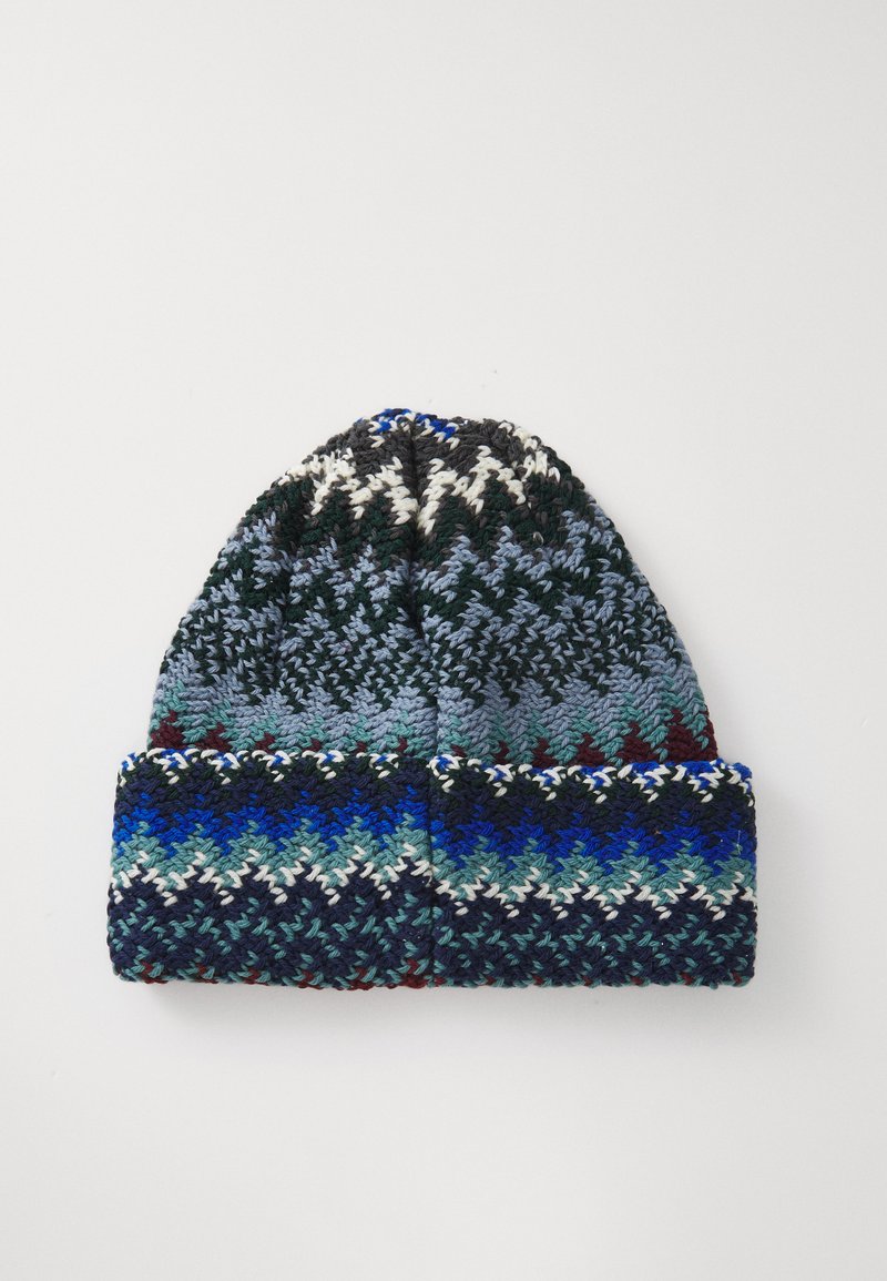 Knitted beanie with a folded brim. Features blue, green, black, and white zigzag patterns. Soft texture with a thick yarn design.