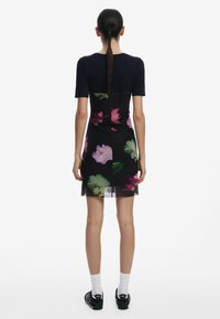 Schwarzes Blumenkleid mit kurzem Ärmel, durchscheinendem Stoff mit rosa und grünen Blumenmustern und einer figurbetonten Silhouette.