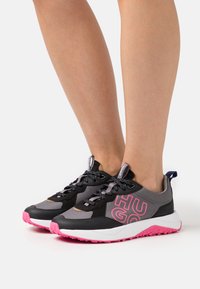 Scarpe sportive nere e grigie con accenti rosa, realizzate in materiale a rete, con logo sul lato, lacci robusti e suola in gomma texturizzata.