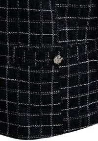 Černá tkanina s tkaným vzorem v kostkovaném designu s bílými nitěmi, s kovovým knoflíkem jako akcentem. Textura vypadá drsně a odolně.