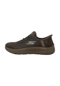Zapatilla deportiva de ante marrón con puntera redondeada, diseño de cordones, suela gruesa y detalles texturizados. Presenta un logo lateral y una marca en el talón.