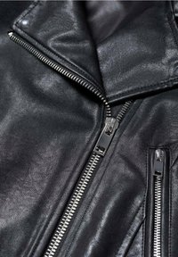 Giubbotto di pelle nera con zip metalliche argentate, una zip diagonale principale parzialmente aperta e una tasca con zip verticale.