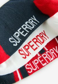 Kolm paari sokke, mis on värvitud segamini tumesinises, valges ja punases. Igal paaril on erinevates värvides ja mustrites broderitud "SUPERDRY".