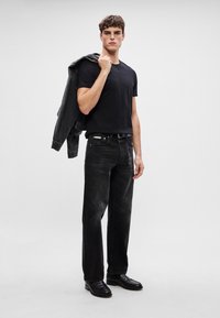 Jachetă neagră din denim peste un tricou negru ajustat, combinată cu blugi negri drepți și pantofi negri lustruiți. Design și textură minimalistă.