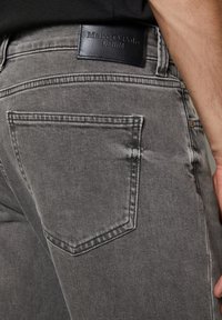 Grijze denim jeans met een achterzak, zichtbare stiksels en een zwart leren label met "Marc O'Polo DENIM" op de tailleband.